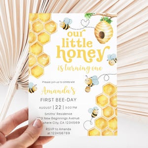May include: A birthday invitation with a bee theme. The invitation features yellow honeycomb patterns, cartoon bees, and the text "Our Little Honey is turning one." The invitation also includes the text "Amanda's First Bee-Day."