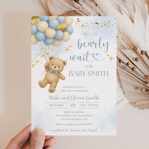 Puede incluir: Invitación a baby shower con un oso de peluche sosteniendo globos azules y dorados. El texto dice "We can bearly wait for Baby Smith". La invitación incluye detalles del evento y efectos de acuarela.