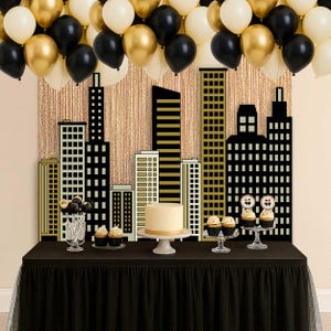 May include: A party scene with black, gold, and white balloons, a cityscape backdrop, and a table with a black skirt. The table holds a cake, cupcakes, and cake pops, all arranged for a celebration.