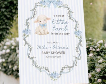 May include: A baby shower sign on a wooden easel. The sign has a light blue striped background and features a lamb illustration with the text "a sweet little lamb is on the way." The sign welcomes guests to Mike + Olivia's baby shower.