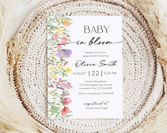 May include: A white baby shower invitation with floral watercolor illustrations. The text reads "BABY in bloom" and includes details for Olivia Smith's baby shower, including the date, time, and location. The invitation is set against a neutral, textured background.