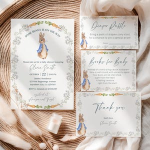 May include: A baby shower invitation suite featuring a watercolor illustration of a bunny in a blue jacket. The invitation includes the text "Some Bunny is on the Way" and details for the event. Additional cards include a diaper raffle, books for baby, and thank you notes.