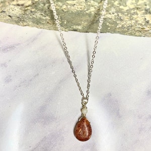May include: A silver chain necklace with a teardrop-shaped pendant made of brown and white stone.
