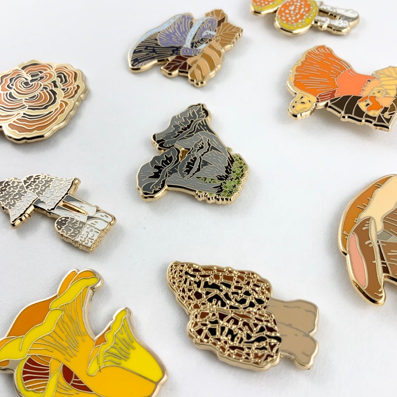 Pu&ograve; includere: Un set di nove spille smaltate che raffigurano diversi tipi di funghi. Le spille sono dorate e presentano una variet&agrave; di colori e disegni, tra cui un fungo marrone e arancione, un fungo bianco e grigio, un fungo nero e verde, un fungo giallo e arancione e un fungo marrone e arancione con un motivo a nido d'ape.