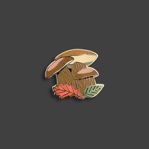 Pu&ograve; includere: Spilla in smalto dorata con tre funghi marroni con accenti rosa e una singola foglia arancione.