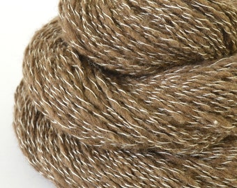 May include: A ball of brown yarn with white flecks. The yarn is tightly wound, showing a textured surface. This yarn is suitable for knitting, crocheting, and other fibre arts projects.