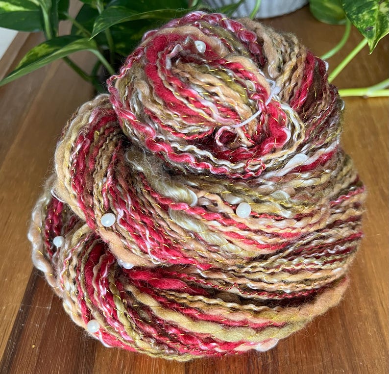 May include: A large ball of colourful yarn with red, gold, cream, and brown fibres. The yarn is speckled with small white beads. The yarn is likely used for knitting or crocheting projects.
