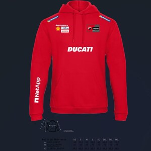 以下が含まれることがあります： フロントポケット付きの赤いドゥカティのパーカー。「DUCATI」の文字が胸に白でプリントされています。ミシュラン、モトローラ、シェル、レノボ、NetAppのロゴも表示されています。パーカーは長袖です。