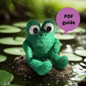 May include: A handmade green frog figurine with large, expressive eyes sits on a rock in a pond. The frog is made of a textured material and has a whimsical appearance. A purple speech bubble with the text "PDF guide" is visible.