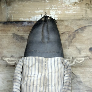 May include: A handmade rag doll with a black fabric head and a striped fabric body. The doll has a simple face with two black eyes and a stitched mouth.