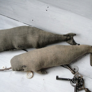 May include: Two gray fabric whale plushies with button eyes. The whales are lying on a white wooden surface with antique keys and buttons scattered around them.  &copy;2015 RavenHive