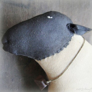 May include: Black and white fabric sheep with a bell around its neck. The sheep has a stitched-on eye and a stitched-on mouth.