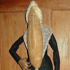 May include: A handmade rag doll with a long, brown nose and white hair. The doll is wearing a black dress with a white lace collar.
