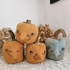 May include: Four handmade fabric pumpkins with embroidered faces. Two are orange and two are blue. The pumpkins are stacked on top of each other.