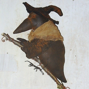 May include: A brown crow with a witch's hat and a burlap scarf is perched on a twig with wire wrapped around it. The crow is holding a twig in its claws.