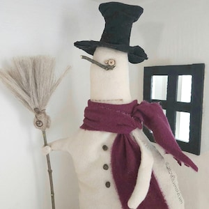 May include: A white snowman with a black top hat, a burgundy scarf, and a twig for a nose. The snowman is holding a broom made of twigs and is standing in front of a window.