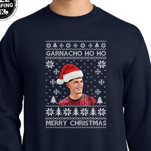 Könnte beinhalten: Ein marineblauer Pullover mit einem weißen Weihnachtspullover-Design, das eine Karikatur eines Fußballspielers mit einem Weihnachtsmann-Hut zeigt. Der Text "GARNACHO HO HO" und "MERRY CHRISTMAS" ist auf dem Pullover gedruckt.