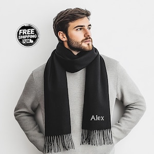 May include: Black cashmere scarf with a personalized embroidered name "Alex" in white thread. The scarf has fringed edges.