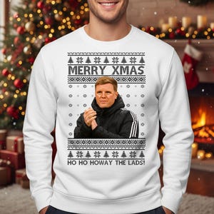 May include: White sweatshirt with a festive design. The sweatshirt features the text "MERRY XMAS" above an image of a man in a black jacket. Below the image is the text "HO HO HOWAY THE LADS!" with snowflake and tree patterns.
