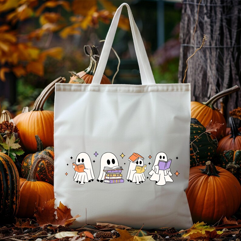 May include: White tote bag featuring a Halloween-themed design. The design includes four cartoon ghosts reading books, with stars and purple diamonds. Pumpkins and fall foliage are in the background.