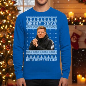 May include: A blue Christmas sweater with the text "MERRY XMAS" and "HO HO HOWAY THE LADS!". The sweater features a portrait of a man in a black jacket. The design includes snowflakes and Christmas trees.