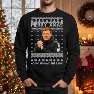 May include: Black sweatshirt with a festive design. The text "MERRY XMAS" is at the top, with a portrait of a man in the center. Below the portrait is the text "HO HO HOWAY THE LADS!" The design includes snowflakes and Christmas trees.