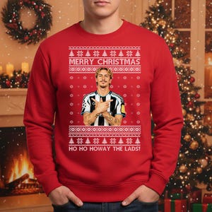 Puede incluir: Jersey navide&ntilde;o rojo con un dise&ntilde;o festivo. El jersey presenta un retrato de un hombre con una camiseta de f&uacute;tbol, con el texto "MERRY CHRISTMAS" y "HO HO HOWAY THE LADS!" en blanco. El dise&ntilde;o incluye copos de nieve y &aacute;rboles de Navidad.