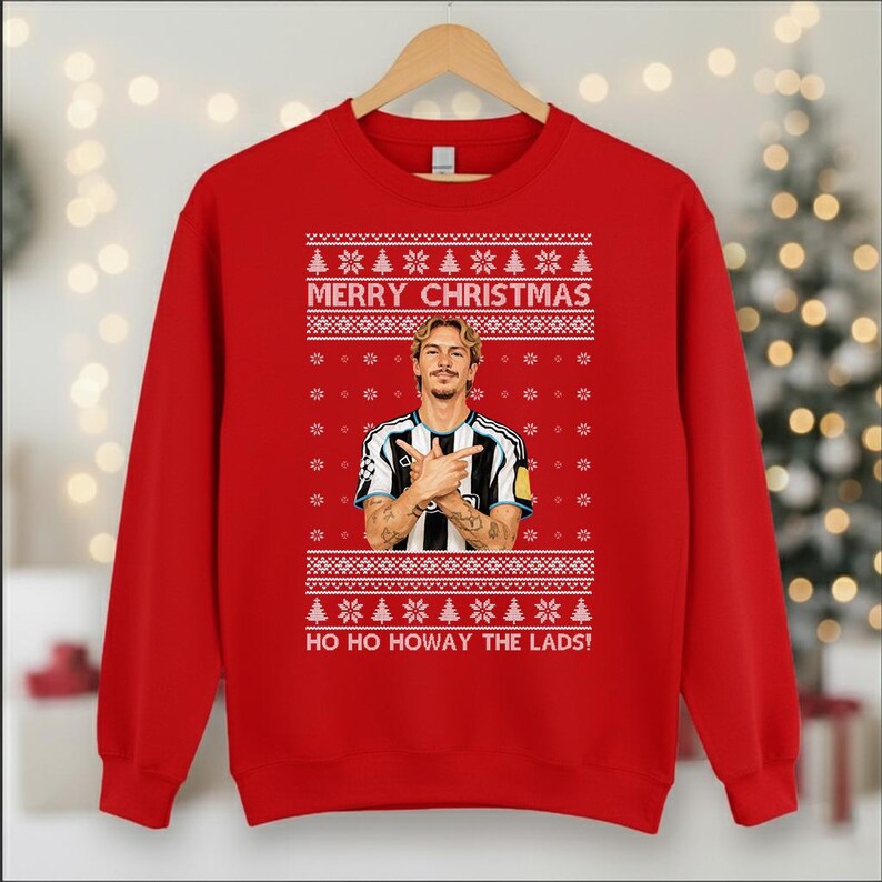 Puede incluir: Una sudadera roja con un dise&ntilde;o festivo. La sudadera presenta el texto "MERRY CHRISTMAS" encima de una imagen de una persona, y la frase "HO HO HOWAY THE LADS!" debajo. El dise&ntilde;o incluye copos de nieve y &aacute;rboles de Navidad.