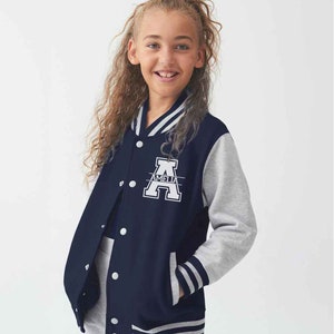 May include: A navy blue varsity jacket with light grey sleeves, featuring a white striped collar, cuffs, and hem. The front displays a large white letter A with the name AMELIA printed horizontally across the centre, and white snap buttons.
