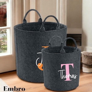 May include: Two grey felt storage bins with handles. The larger bin has an orange design and the smaller bin has a pink letter T and the name Thomas in white.