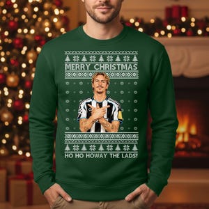 Puede incluir: Jersey navide&ntilde;o verde oscuro con un dise&ntilde;o festivo. El jersey presenta el texto "MERRY CHRISTMAS" y "HO HO HOWAY THE LADS!". Tambi&eacute;n incluye un gr&aacute;fico de una persona con una camiseta a rayas blancas y negras. El jersey es de cuello redondo.