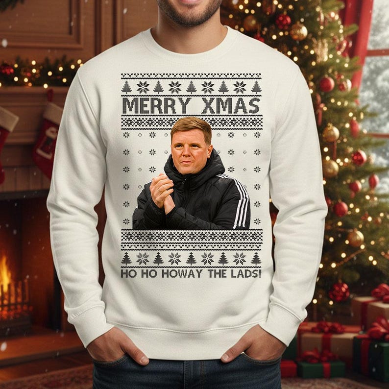 May include: Cream-colored Christmas sweater with a festive design. The sweater features the text "MERRY XMAS" above an image of a man in a black jacket. Below the image is the text "HO HO HOWAY THE LADS!" The sweater has a crew neck and long sleeves.