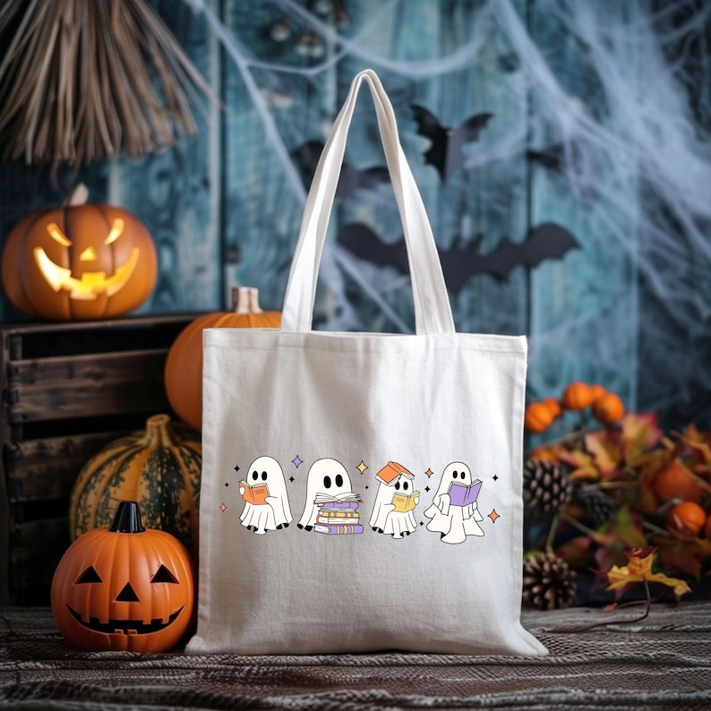 May include: A white canvas tote bag featuring a Halloween-themed design of cartoon ghosts reading books. The bag has long handles and is surrounded by carved pumpkins, gourds, and fall foliage, creating a festive autumn scene.