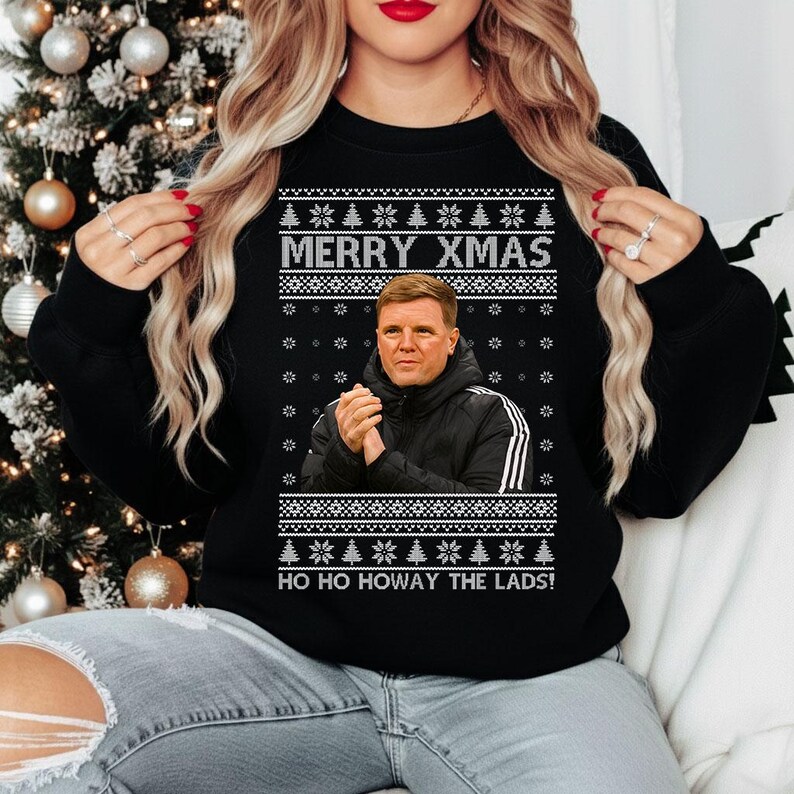 May include: Black sweatshirt with a festive design. The sweatshirt features the text "MERRY XMAS" above an image of a man in a black jacket. Below the image is the text "HO HO HOWAY THE LADS!" The design includes white snowflakes and Christmas tree patterns.
