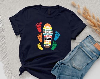 May include: Navy blue t-shirt with a colorful graphic design for Father's Day. The design includes footprints in various colors and the text "HAPPY FATHER'S DAY TO THE BEST DAD WE LOVE YOU".