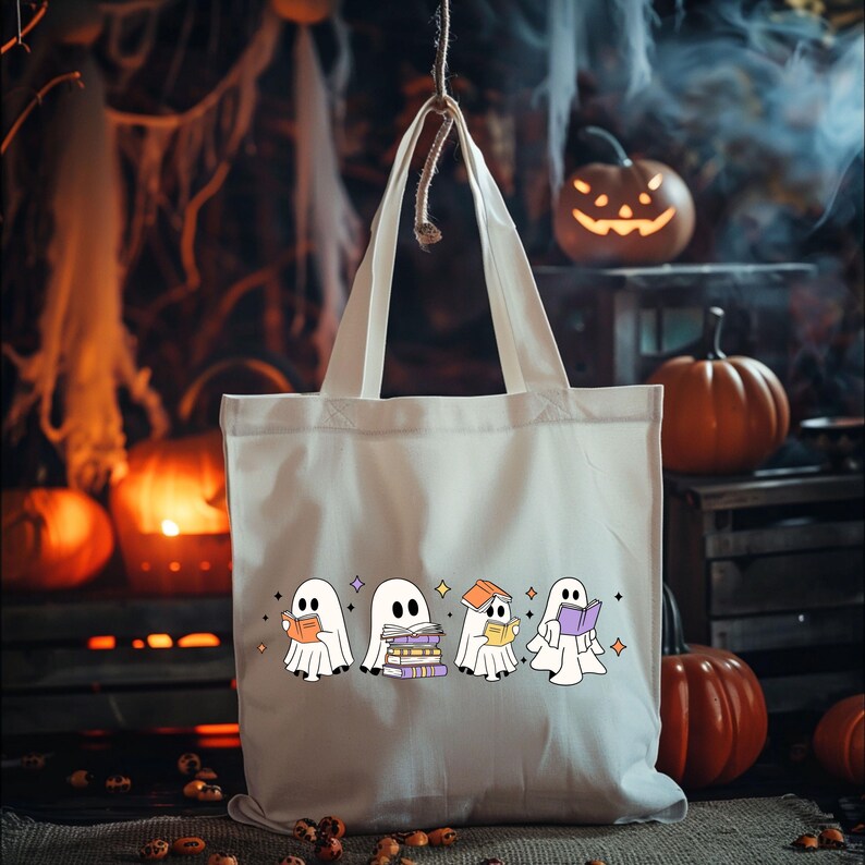 May include: Off-white tote bag featuring a row of cartoon ghosts reading books. The ghosts are white with black eyes and are holding books of various colors. The background includes pumpkins and Halloween decorations.