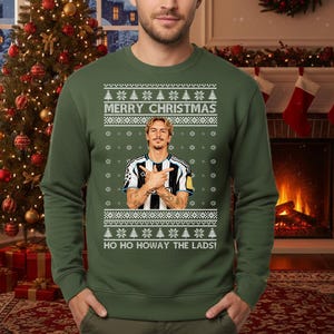 Puede incluir: Jersey navide&ntilde;o verde con un dise&ntilde;o festivo. El jersey presenta el texto "MERRY CHRISTMAS" y "HO HO HOWAY THE LADS!" junto con un gr&aacute;fico de una persona. El jersey tiene cuello redondo y mangas largas.