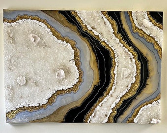 May include: A large abstract painting with a white, gray, black, and gold agate design. The painting is hanging on a white wall above a black cabinet with glass doors.
