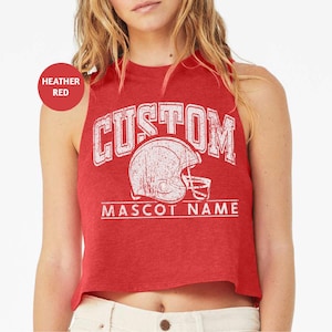 May include: A heather red cropped tank top with a white vintage-style graphic of a football helmet and the text "CUSTOM MASCOT NAME".