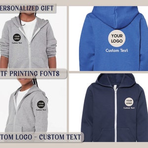 May include: A personalized gray zip-up hoodie with a black circle containing the text "YOUR LOGO" and the words "Custom Text" below. The hoodie is shown on a child model. The image also shows a blue zip-up hoodie with the same design. The text "10 DTF PRINTING FONTS" is displayed above the image. The text "CUSTOM LOGO - CUSTOM TEXT" is displayed below the image.