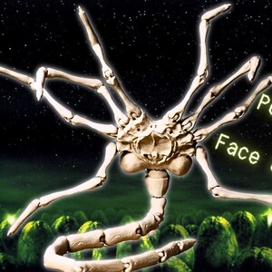 May include: A white, articulated, plastic model of the facehugger from the Alien movie franchise. The model is posed with its arms outstretched and its tail curled underneath. The model is set against a backdrop of green alien eggs and a starry night sky. The text "Poseable Face Grabber" is written in white on a black background.