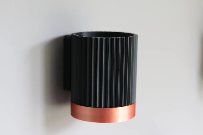 May include: A black and copper wall-mounted cup holder with a ribbed design.
