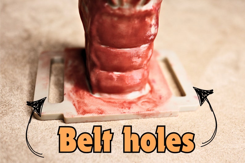 May include: Close-up of a white plastic belt buckle with two belt holes. The buckle is stained red.