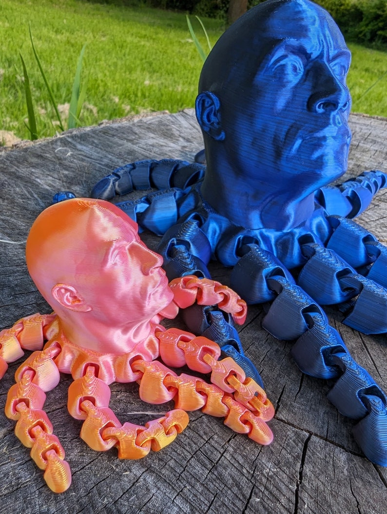 May include: Two 3D printed octopus sculptures, one blue and one orange, with human heads. The octopus tentacles are made of linked chain-like segments.
