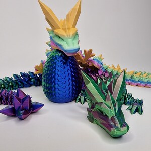 May include: A 3D printed iridescent dragon figurine with a blue egg and a green head. The dragon's tail is made of individual crystal-like scales.