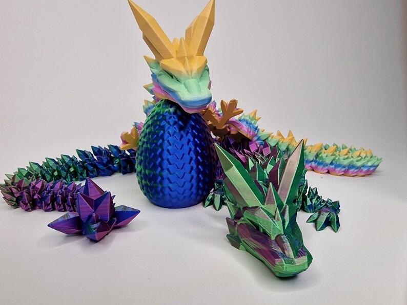 May include: A 3D printed iridescent dragon figurine with a blue egg and a green head. The dragon's tail is made of individual crystal-like scales.