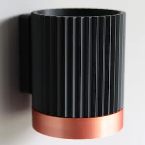 May include: A black and copper cylindrical wall-mounted toothbrush holder with a ribbed design.