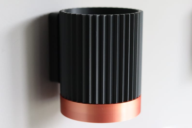 May include: A black and copper cylindrical wall-mounted toothbrush holder with a ribbed design.
