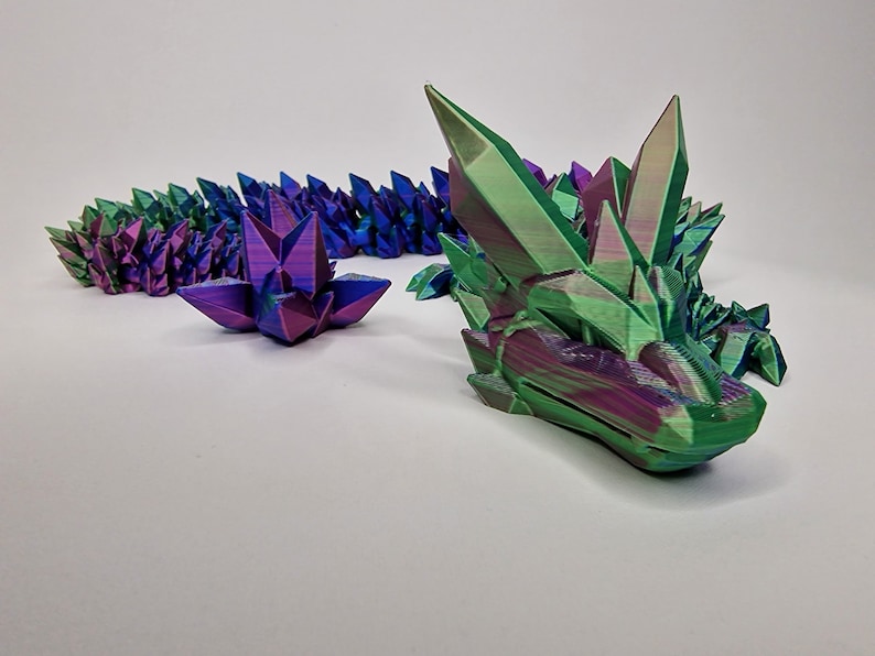 May include: A 3D printed iridescent dragon sculpture with a green and purple color scheme. The dragon is made up of many small, pointed crystals.