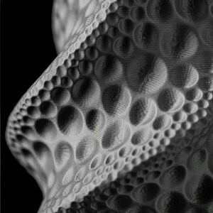 May include: Abstract grayscale sculpture with a textured surface. The design features a repeating pattern of rounded shapes, creating a dynamic and visually engaging form. The piece has a modern aesthetic and is set against a black background.